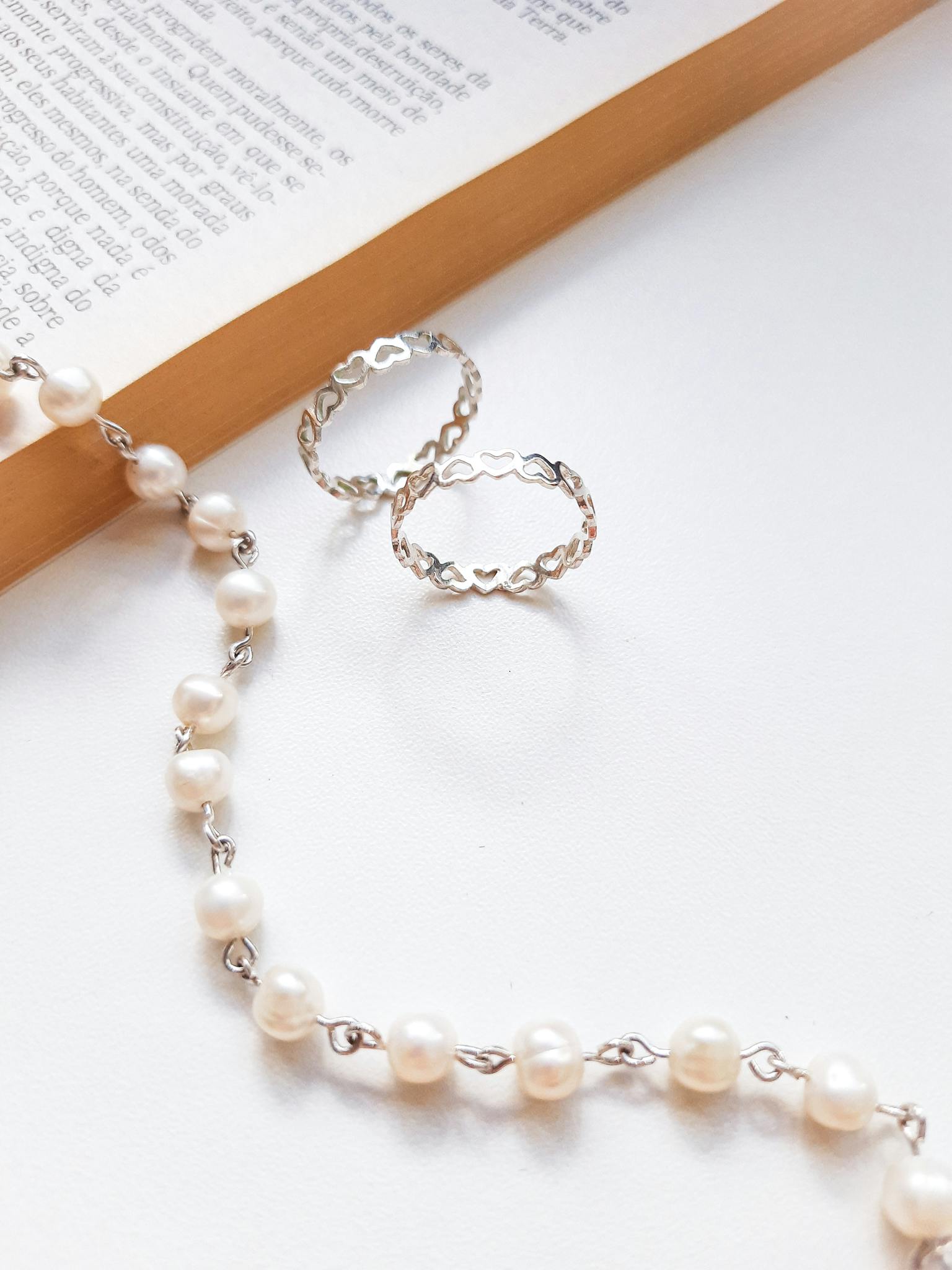 A delicate arrangement of pearl necklace and silver rings on the pages of an open book, exuding elegance.