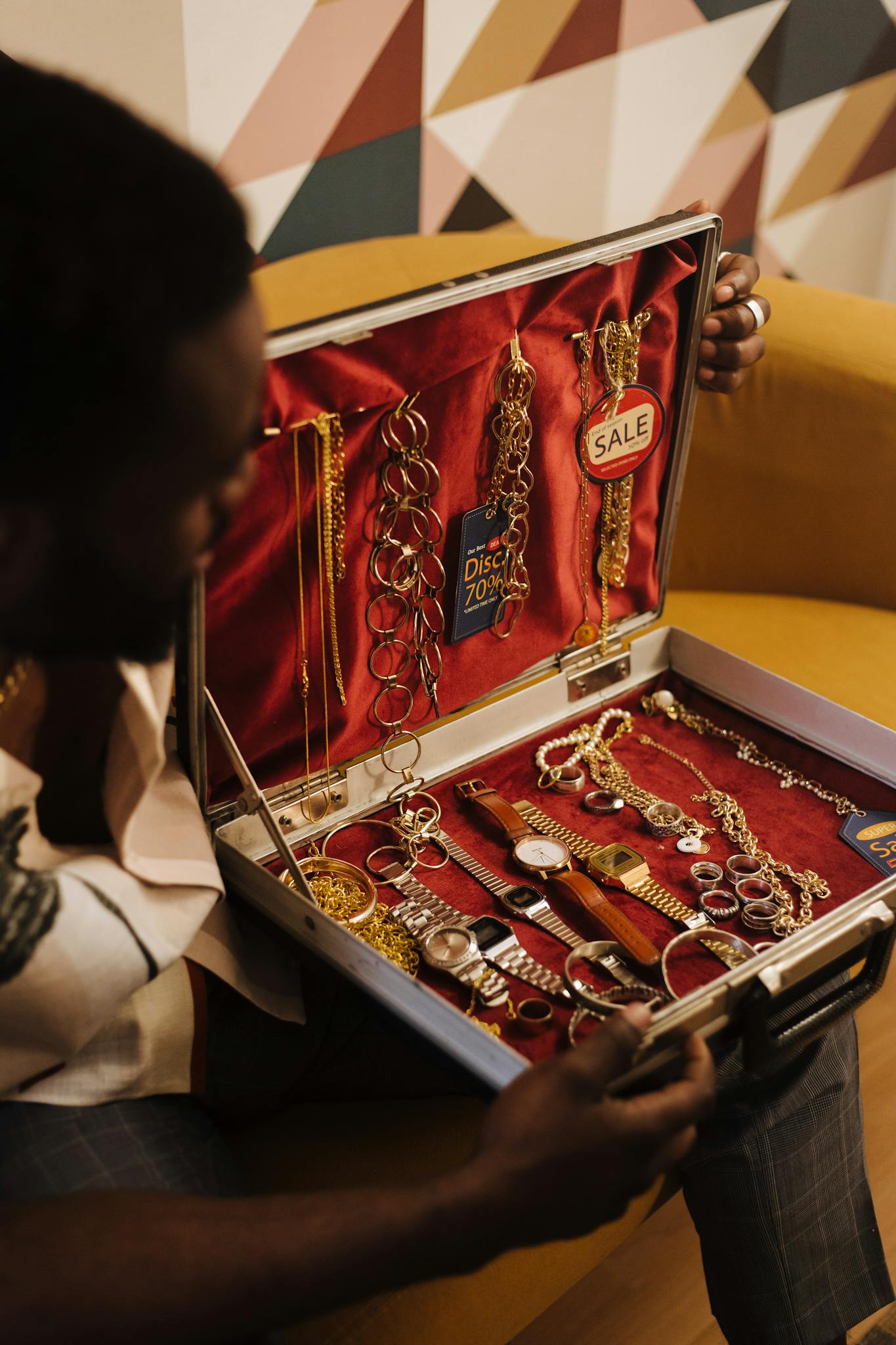 A person showcases a variety of jewelry and watches in an open briefcase indoors.